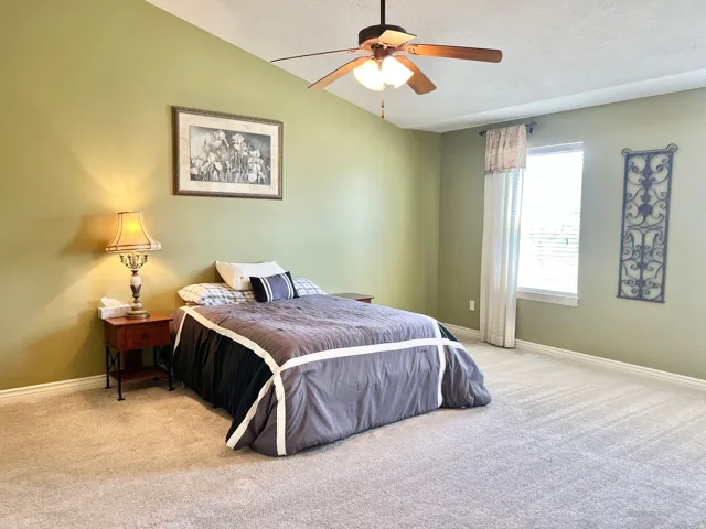 Spacious room featuring vaulted ceilings, a ceiling fan, light-colored carpet flooring, a window with blinds, and light green walls