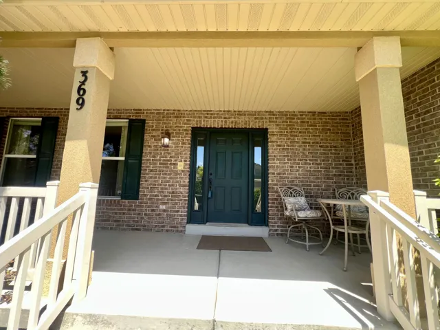 Inviting front porch featuring brick siding and a dark green entry door with sidelights