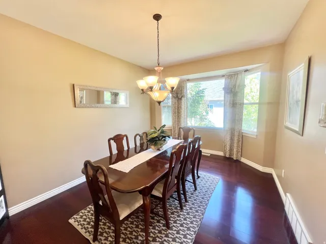 Formal dining space featuring dark wood-finish flooring, a bay window with natural light, and a prominent chandelier