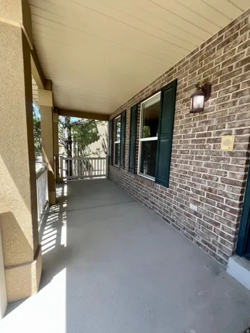 Covered front porch featuring a brick facade, decorative wall sconce, and dark green louvered shutters