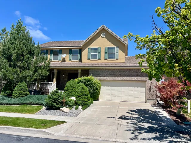 Two-story stucco and brick exterior featuring a covered front porch, an attached two-car garage, mature landscaping, and a concrete driveway