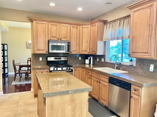 Kitchen featuring recessed lighting, honey-toned cabinetry with crown molding, stainless steel appliances, and a tiled island