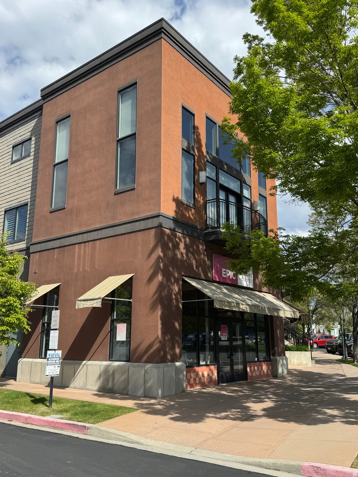 Corner commercial building featuring a stucco exterior, multiple storefront windows with awnings, and a second-story balcony with iron railings