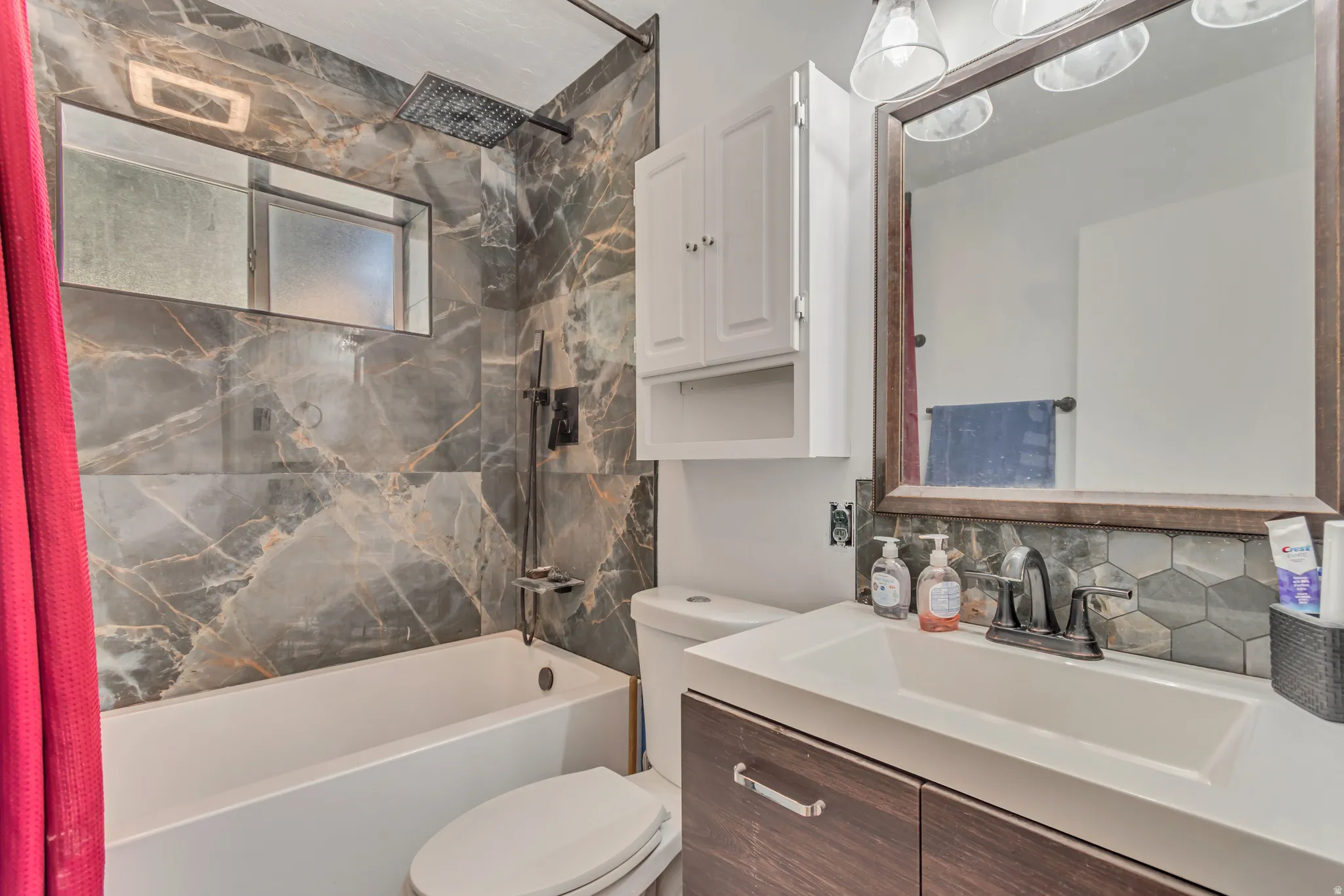 Bathroom featuring a shower-over-tub combination with large format marbled tile surround, a rainfall showerhead, and an integrated window