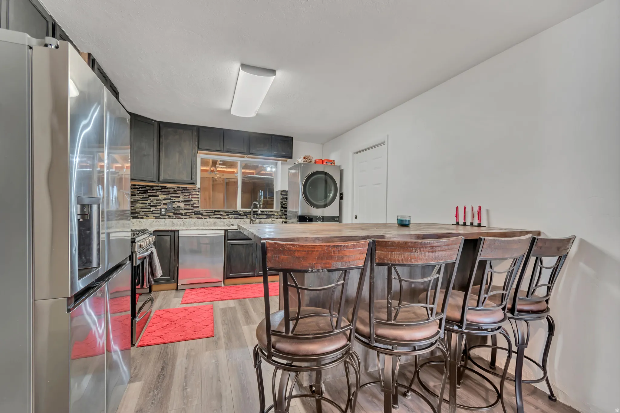 Kitchen featuring a built-in wood-finish breakfast bar, stainless steel appliances, dark cabinetry, and a multi-tone backsplash