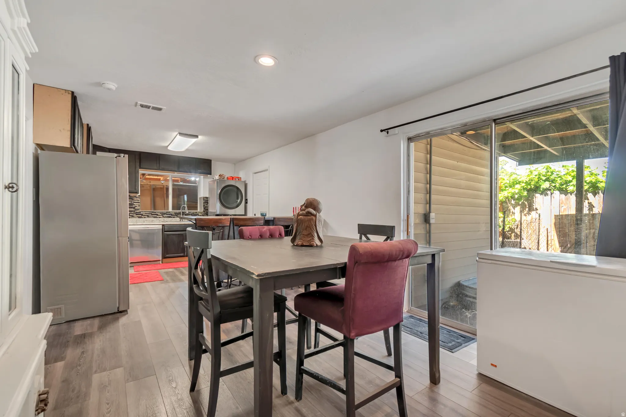 Open-concept kitchen and dining area featuring wood-finish flooring, dark cabinetry, and a tile backsplash