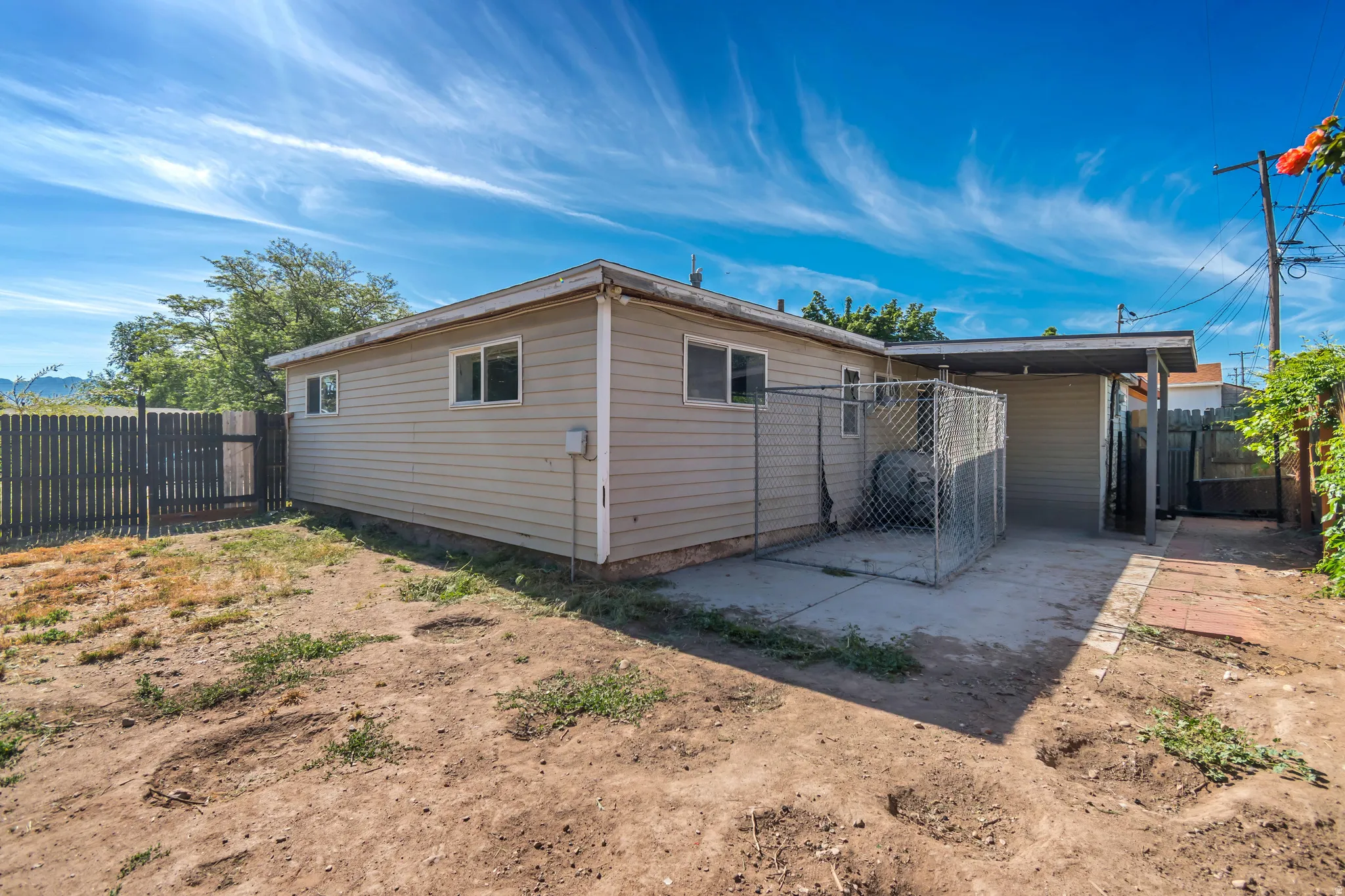 Rear exterior featuring a covered patio, chain-link enclosure, and a picket fence