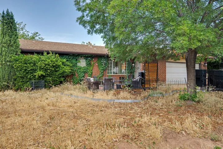 Brick exterior featuring a front patio area, mature trees, and an attached garage with a metal garage door