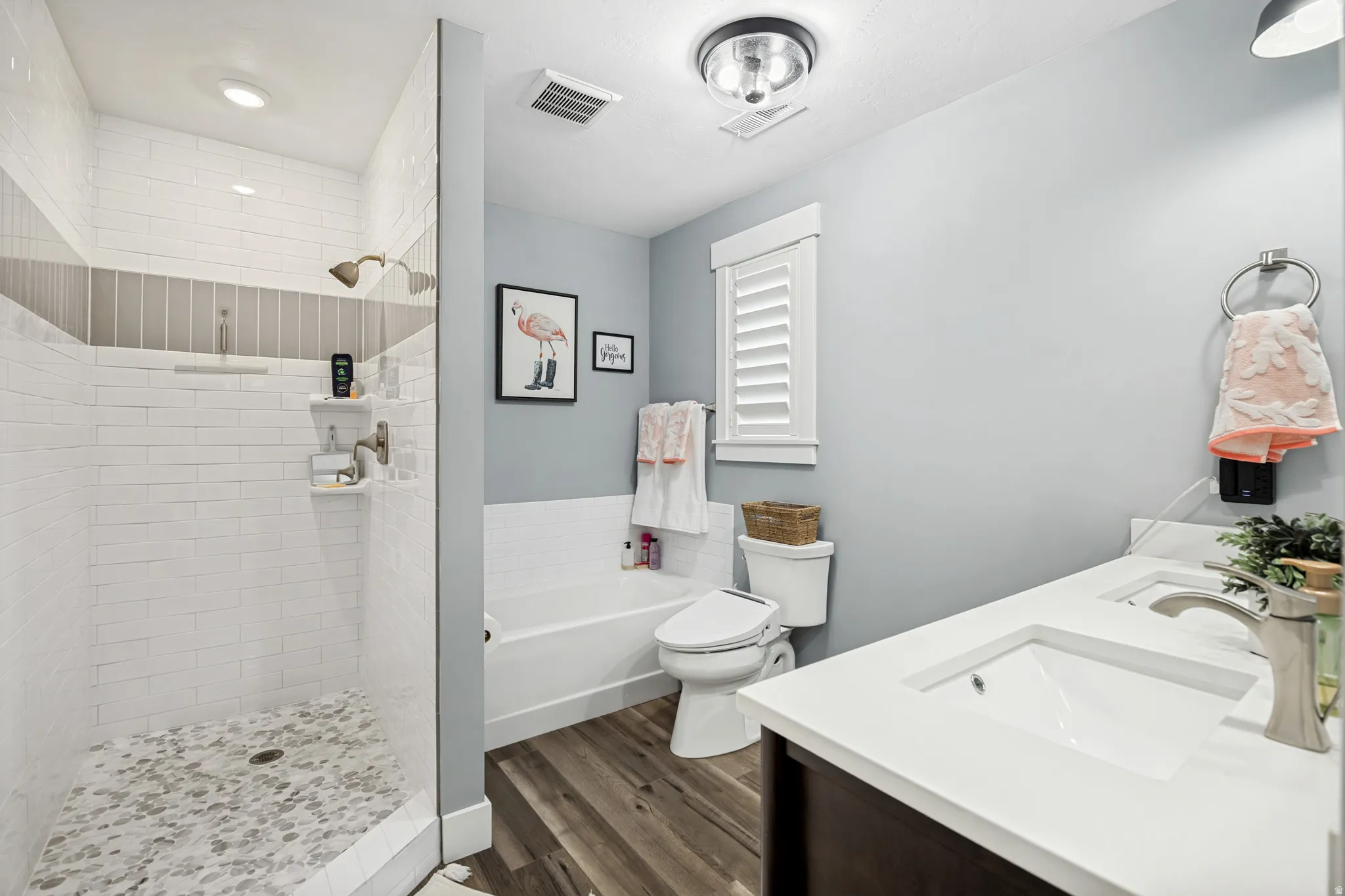 Bathroom featuring a walk-in shower with subway tile and a decorative mosaic band, a separate bathtub, and a dual-sink vanity with a white countertop