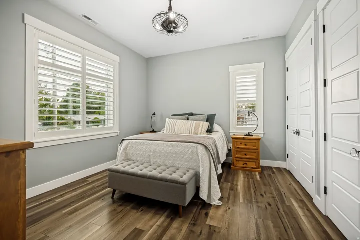 Bedroom featuring wood-finish flooring, two windows with white plantation shutters, and a modern ceiling fixture