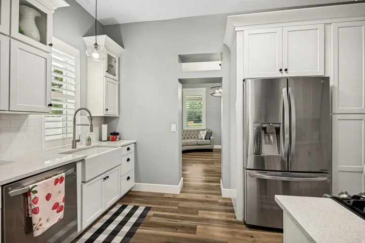 Contemporary kitchen featuring white shaker cabinetry, quartz countertops, a farmhouse sink, stainless steel appliances, and wood-finish flooring