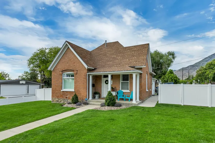 Brick exterior home featuring a covered front porch with white columns, a pitched shingle roof, and a concrete walkway