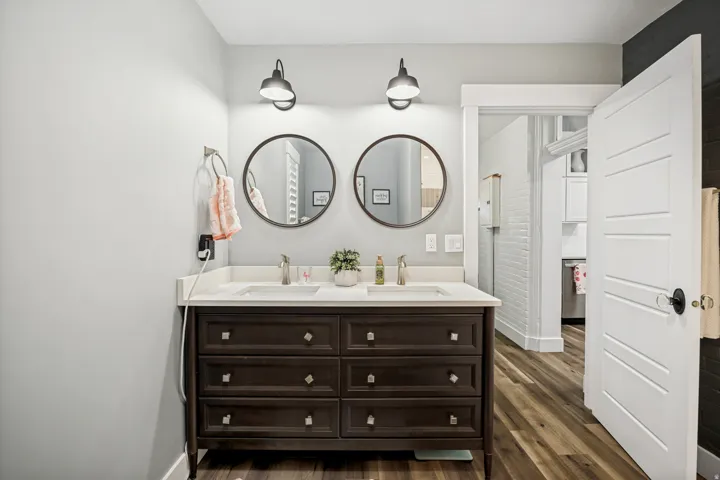Bathroom featuring a dual vanity with a dark wood-finish cabinet and white countertop, two circular mirrors, and industrial-style wall sconces