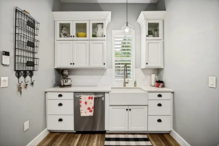 Kitchenette featuring white shaker cabinetry, white subway tile backsplash, a stainless steel dishwasher, a farmhouse sink, and wood-finish flooring