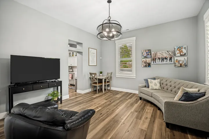 Open-concept living space featuring wood-finish flooring, a modern drum pendant light, and crisp white trim around windows