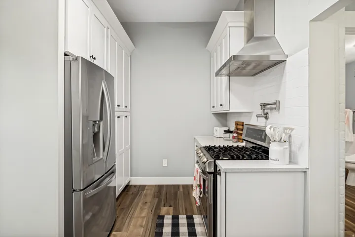 Galley kitchen featuring white shaker cabinetry, stainless steel appliances, a pot filler, and wood-finish flooring