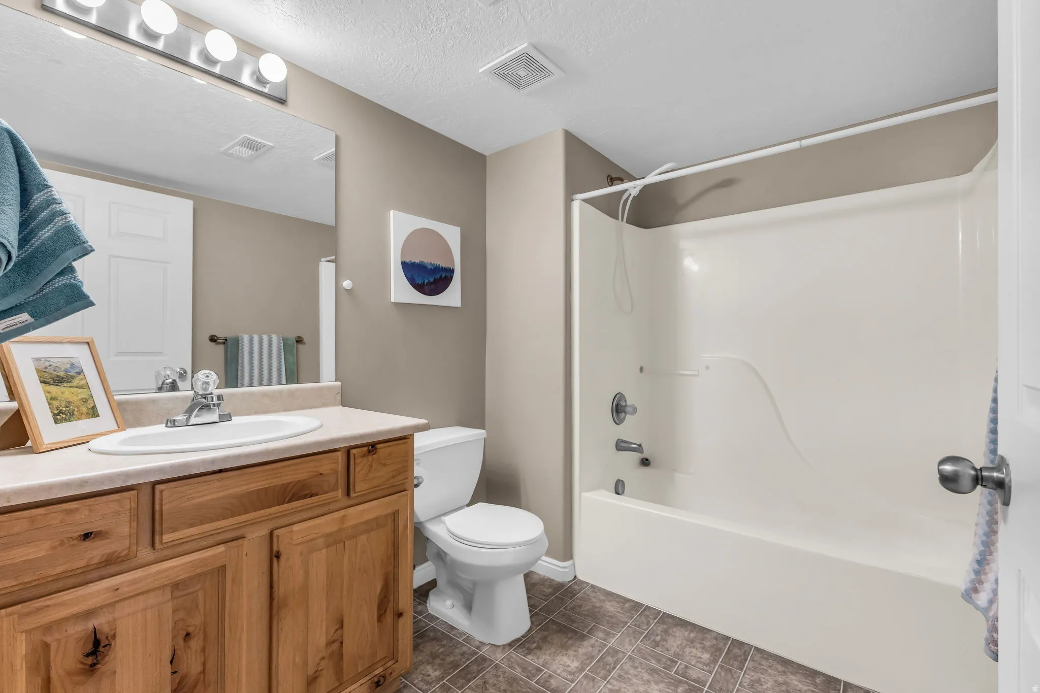Bathroom featuring a wood-finish vanity with a built-in sink, a standard toilet, and a combined shower-tub unit