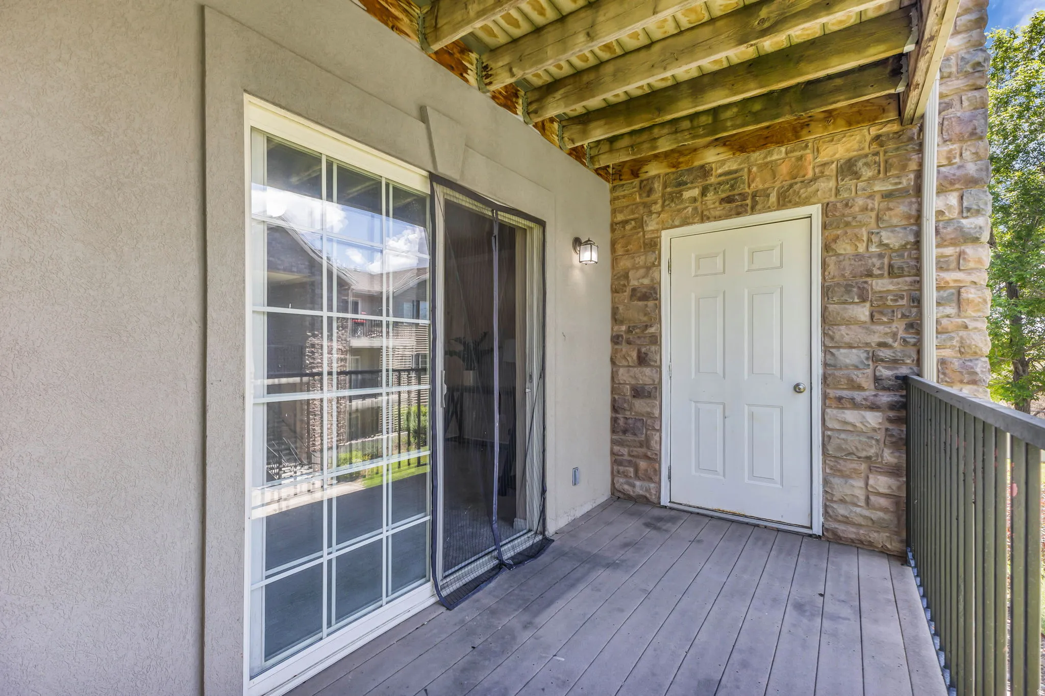 Outdoor deck featuring plank flooring, stone veneer accent wall, white paneled door, and sliding glass door with grid pattern