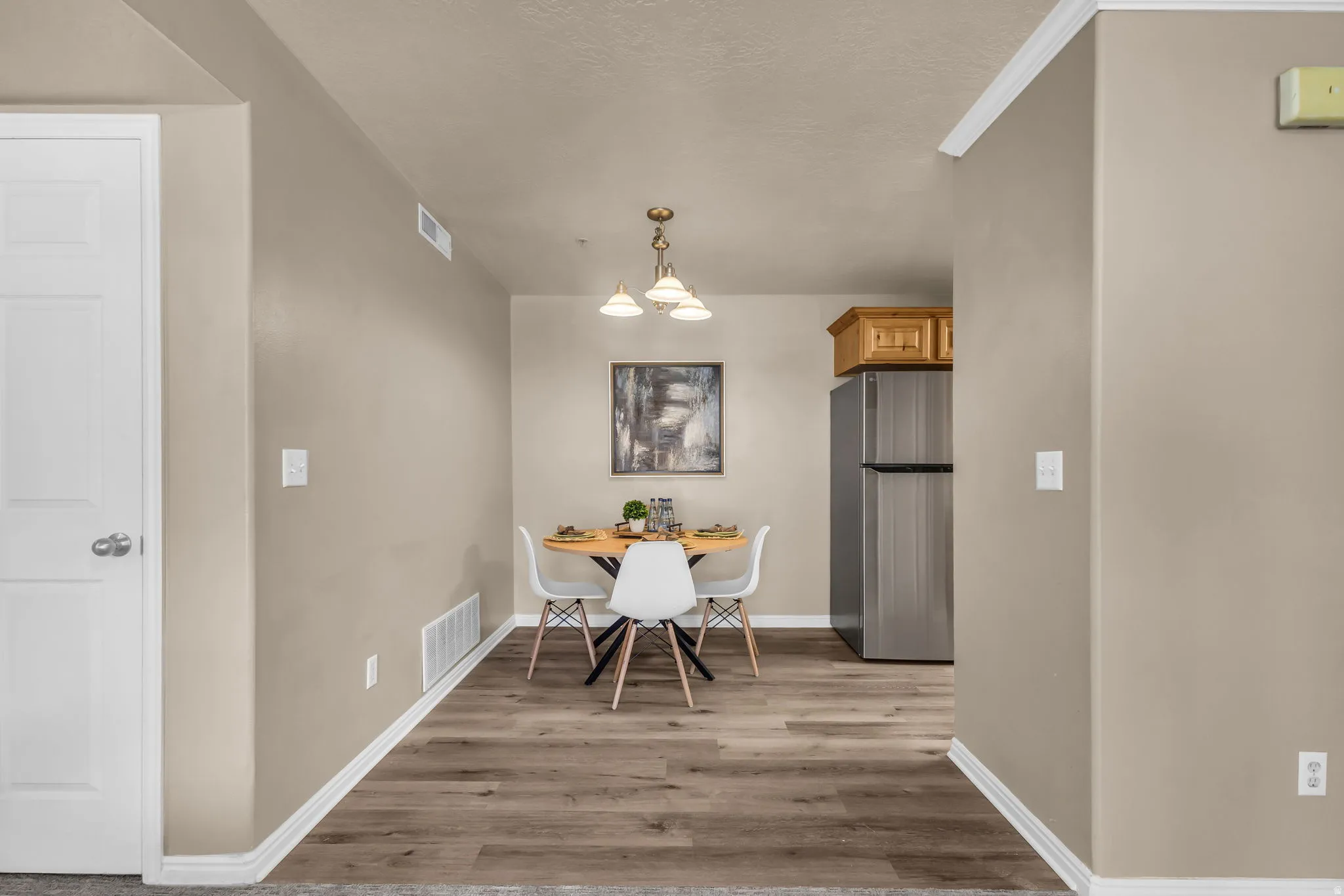Open dining area with wood-finish flooring, complemented by a brushed nickel chandelier