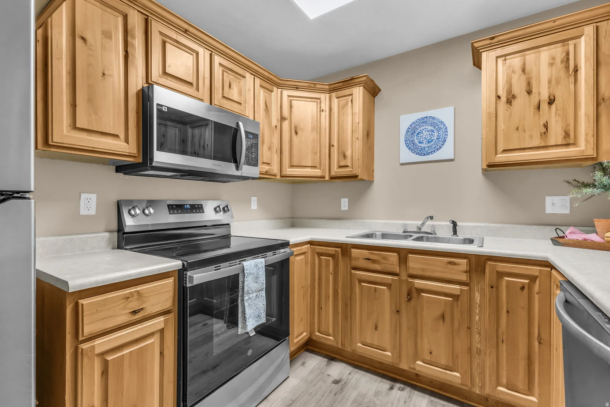 Kitchen featuring natural wood-finish cabinetry, light-toned countertops, stainless steel appliances, and wood-finish flooring