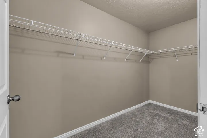 Spacious walk-in closet featuring light beige walls, white wire shelving, and grey carpet flooring