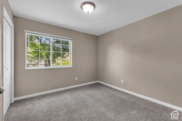 Room featuring neutral wall tones, gray carpet flooring, a large window with white trim, and a flush mount ceiling light
