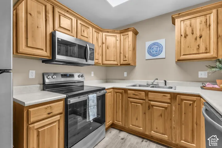 Kitchen featuring natural wood-finish cabinetry, light-toned countertops, stainless steel appliances, and wood-finish flooring
