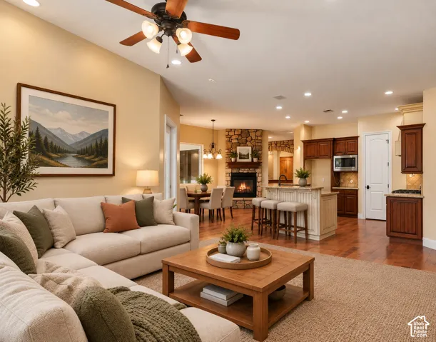 Open-concept interior featuring vaulted ceilings, wood-finish flooring, a stone-surround corner fireplace, recessed lighting, and built-in stained-wood cabinetry