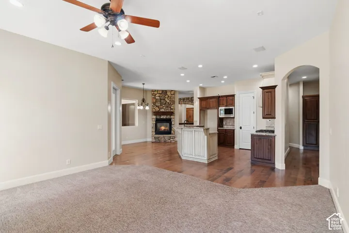 Spacious interior featuring a stone-clad fireplace, wood-finish flooring, recessed lighting, a ceiling fan, and an arched entryway