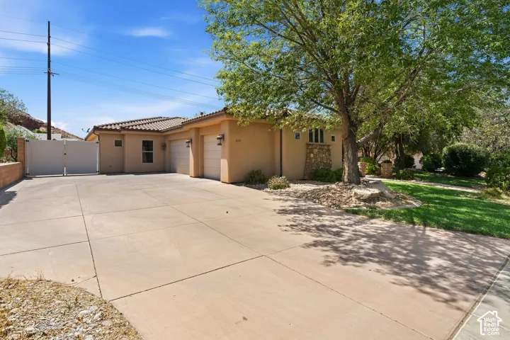 Stucco exterior with a tile roof, featuring a two-car garage with individual doors, a large concrete driveway, and a stone accent wall