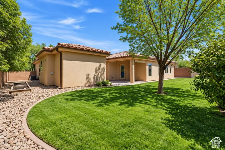 Stucco exterior with a tiled roof, featuring a covered patio, manicured lawn, rock landscape borders, and masonry perimeter wall