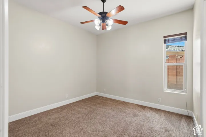 Carpeted room featuring a ceiling fan with light fixture, window with blinds, and white baseboards