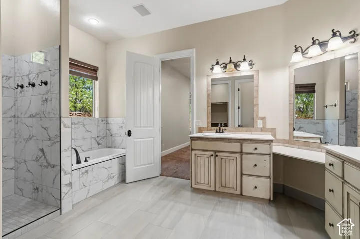 Spacious bathroom featuring tiled flooring, a built-in soaking tub with surround tiling, a glass-enclosed shower with tiled walls, and dual vanity areas with integrated sinks and custom cabinetry