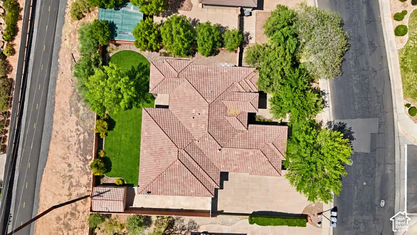 Aerial perspective of property featuring a tile roof, concrete driveway, fenced perimeter, mature landscaping, and manicured lawn