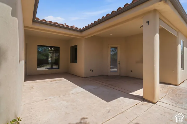 Expansive covered patio featuring stucco walls, tiled roof, concrete flooring, large window, and a glass-paneled door
