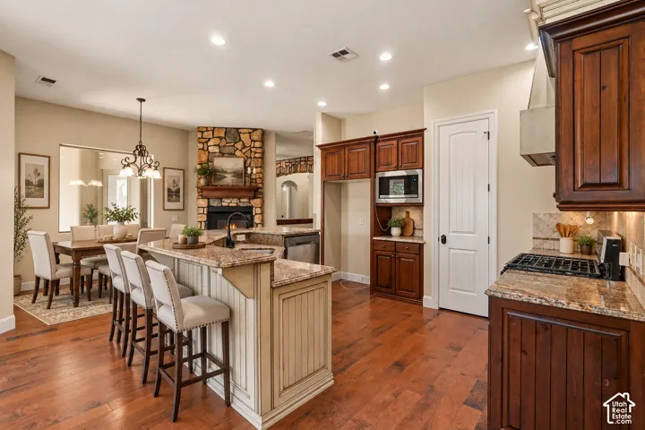 Kitchen featuring dark wood cabinetry, stone-finish countertops, wood-finish flooring, recessed lighting, and a corner stone-surround fireplace