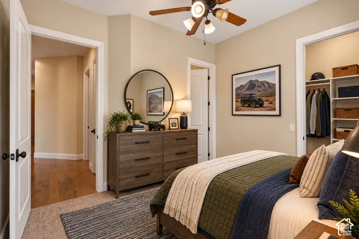 Neutral interior featuring carpeted flooring, wood-finish flooring, a ceiling fan with light fixture, and walk-in closet with built-in shelving
