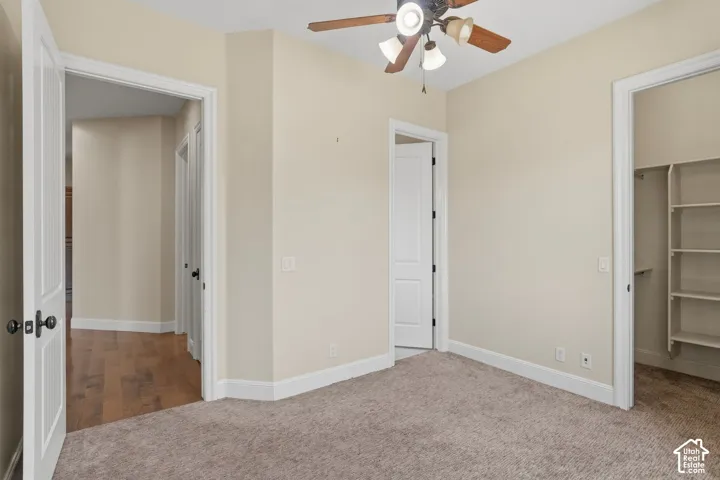 Carpeted room featuring a ceiling fan with integrated lighting, multiple doorways, and a closet with built-in shelving