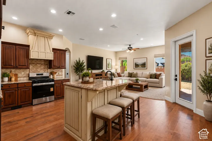 Open-concept kitchen featuring stained wood cabinetry, stone countertops, a center island with beadboard detailing, recessed lighting, and wood-finish flooring