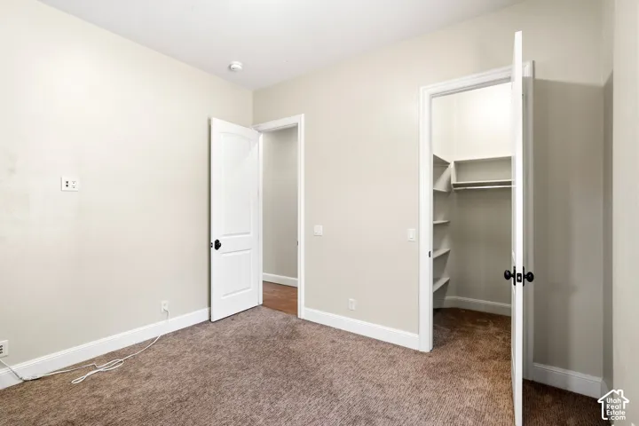 Neutral-toned room featuring plush brown carpeting, a built-in closet with shelving and hanging rod, white trim, and a white paneled door with black hardware