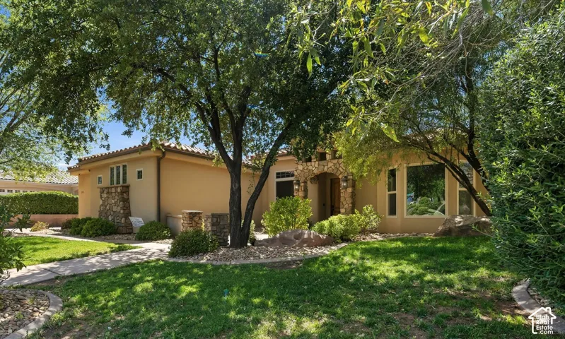 Single-story exterior featuring stucco siding, stone masonry accents, tile roofing, and mature landscaping