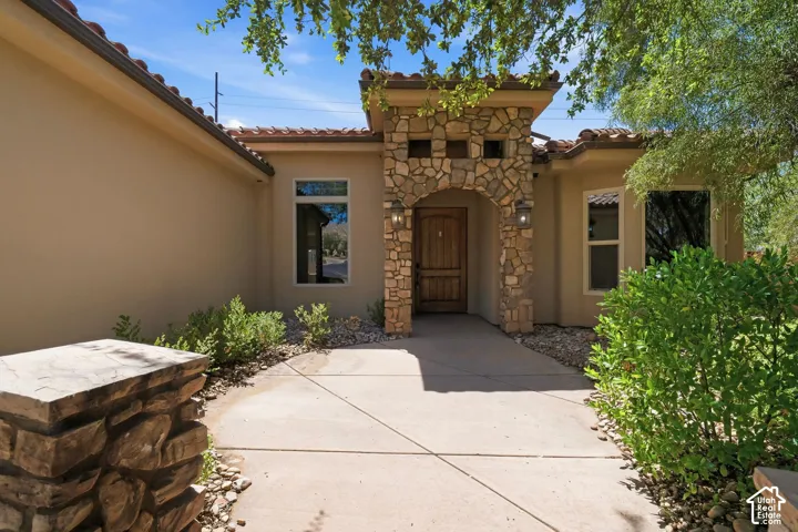 Stucco exterior with a stone archway entry and a wood front door, complemented by a concrete walkway, tile roofing, and low-maintenance landscaping