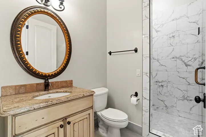Bathroom featuring a distressed wood-finish vanity with a stone countertop, an oval mirror, and a glass-enclosed shower with marble-look tile