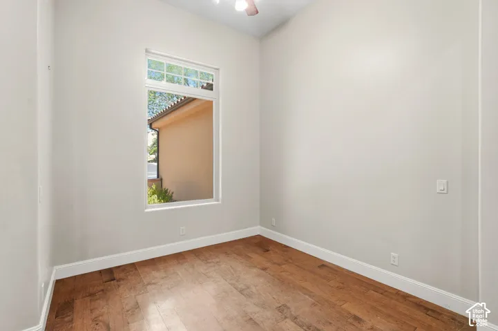 Room featuring wood-finish flooring, a single window with transom, white baseboards, light-toned wall paint, and a ceiling fan