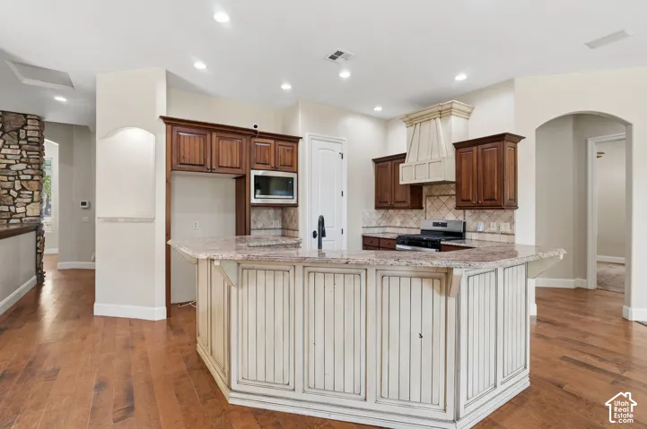 Kitchen featuring a multi-level island with stone-look countertops, rich wood cabinetry, integrated microwave, and a decorative range hood