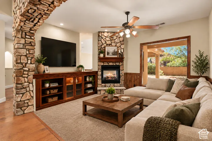 Living area featuring a floor-to-ceiling stone-faced fireplace with a wood mantel, a prominent arched stone entryway, built-in wooden cabinetry, recessed lighting, and wood-finish flooring