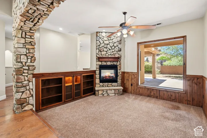 Stone-clad fireplace with wood mantle and hearth, built-in cabinetry with glass doors, wood-finish wall paneling, and a stone archway