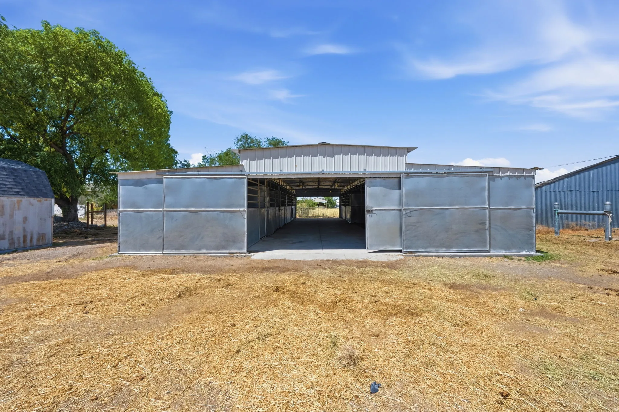 Open-air metal barn structure with multiple stalls, a wide central aisle, and a metal roof