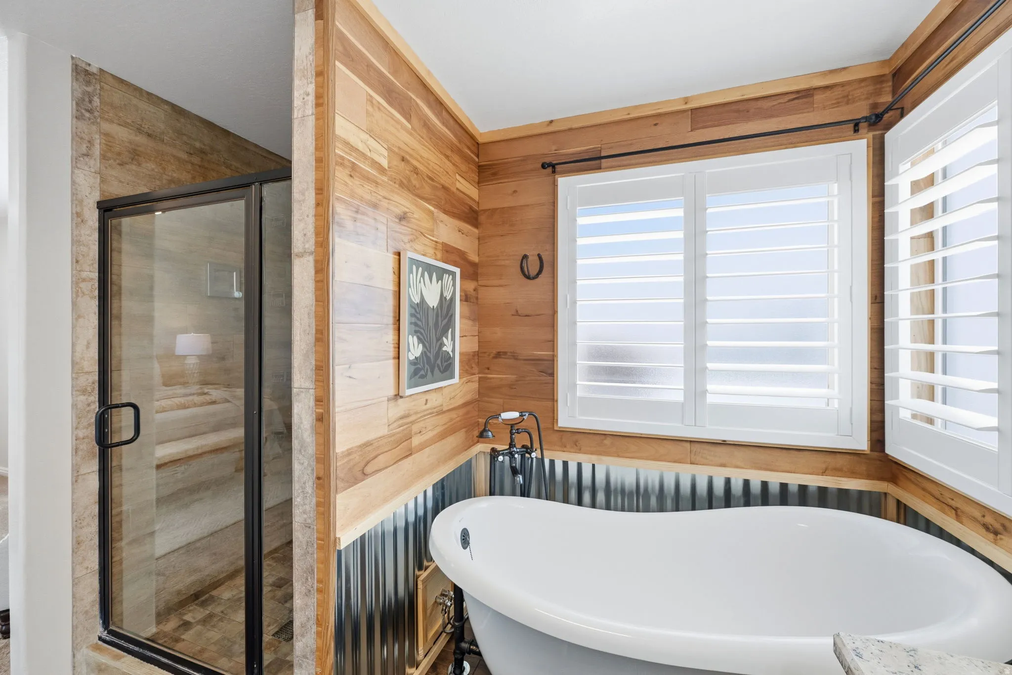 Freestanding soaking tub with dark bronze fixtures, wood-paneled walls, and white plantation shutters