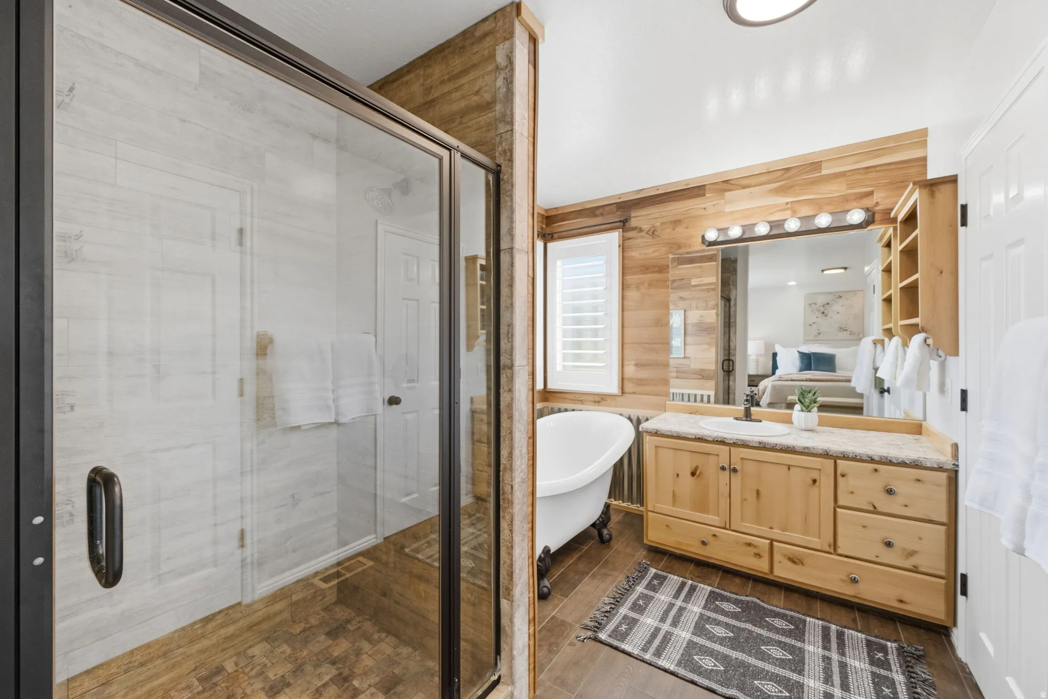 Bathroom featuring a glass-enclosed shower, freestanding clawfoot tub, wood-finish flooring, wood plank accent walls, and a vanity with natural wood cabinetry and stone-finish countertop